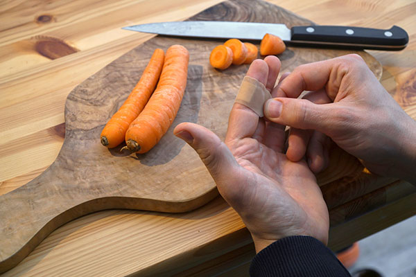 Eine Person wickelt sich ein Pflaster um den Finger, an dem sie sich beim Karottenschälen geschnitten hat.