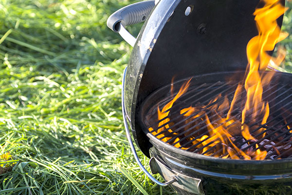 Ein Kugelgrill mit brennenden Kohlen steht auf einer Wiese.